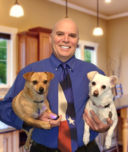 Gary Henicke, Texas REALTOR, smiling in a blue shirt and Texas flag tie holding his small dogs Little Boy and Chispa.