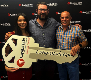 Gary Henicke standing with excited first-time homebuyers holding a giant congratulations key on closing day in Corpus Christi, Texas.